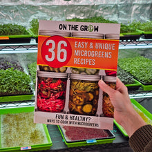 Cargar imagen en el visor de la galería, On The Grow 36 Easy and Unique Microgreens Recipes cookbook held in front of microgreens growing on shelves