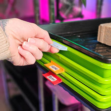 Load image into Gallery viewer, On The Grow microgreen tray clip labelers in multiple colors clipped to stacked Bootstrap Farmer trays on a grow rack