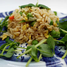 Load image into Gallery viewer, A mound of fried rice with peas, scrambled egg bits, and diced vegetables is garnished with fresh green microgreens, served on a blue and white patterned plate.