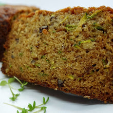 Load image into Gallery viewer, A thick slice of zucchini bread with visible green zucchini flecks and small dark nuts, garnished with delicate microgreens, sits against a white background.