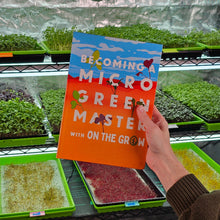Cargar imagen en el visor de la galería, Person holding a book titled 'Becoming a Microgreen Master with On The Grow' in a greenhouse setting
