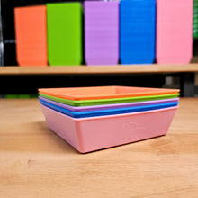 Load image into Gallery viewer, Five Bootstrap Farmer 5x5 shallow microgreen trays in assorted colors stacked on a wood surface with individual trays standing behind
